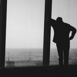 Un homme de dos, debout devant une grande baie vitrée, en noir et blanc